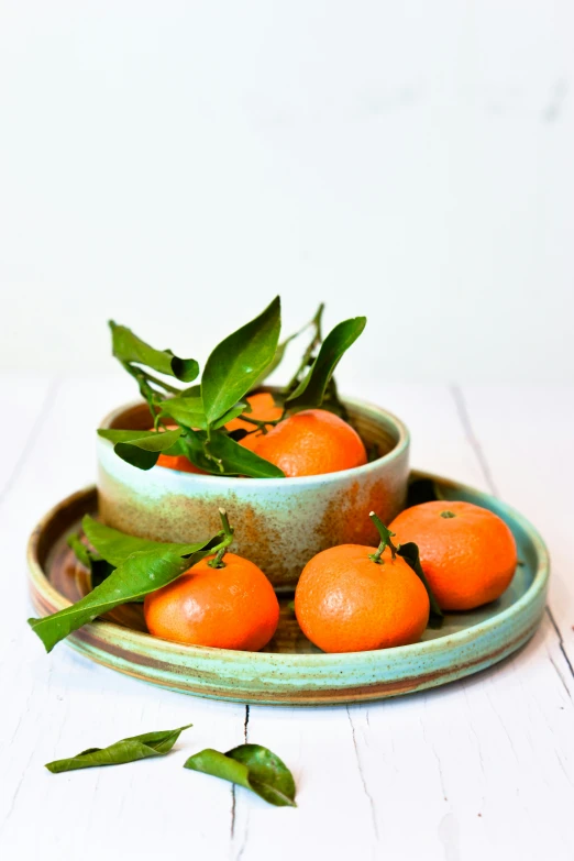 a plate of oranges is on a table with leaves