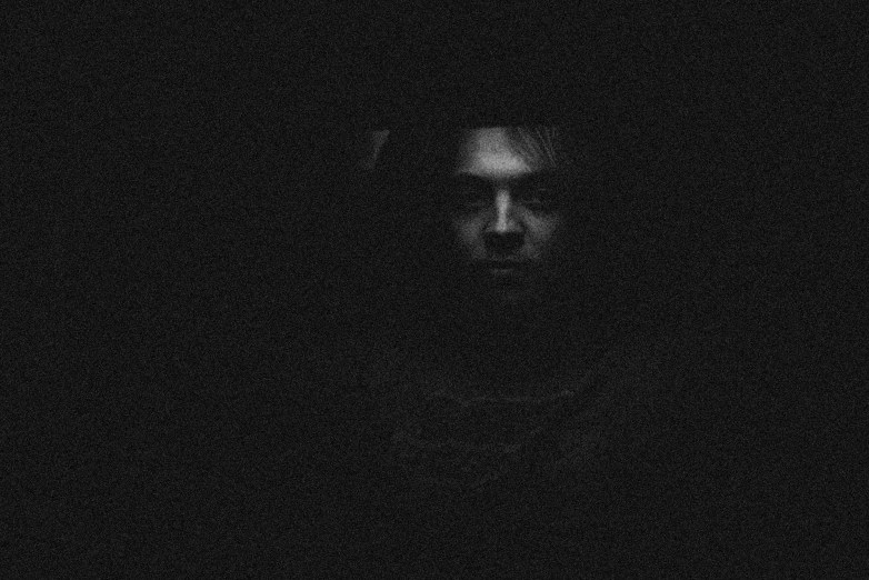 a man in a black shirt and tie standing in a dark room