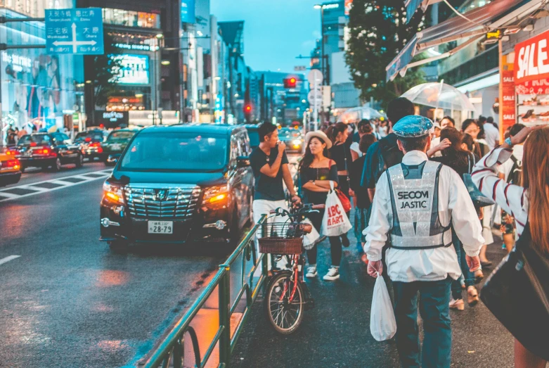 a group of people walking down a sidewalk past cars