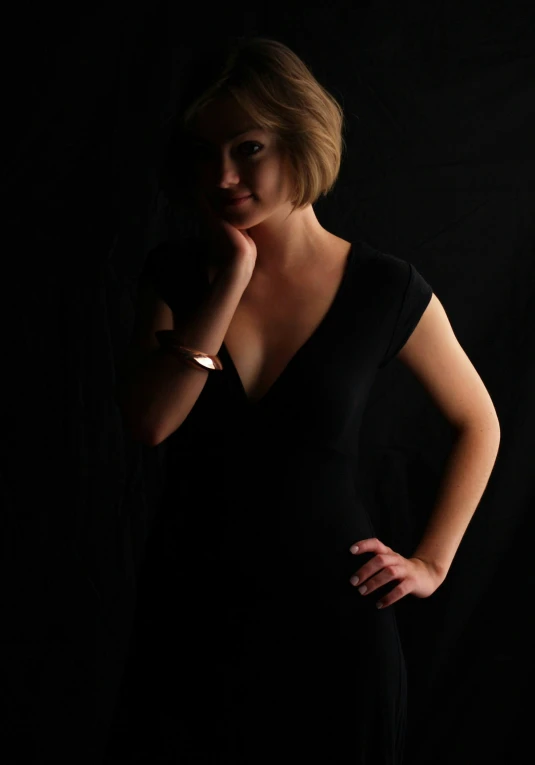 the woman is posing in a black dress with her hands on her cheek