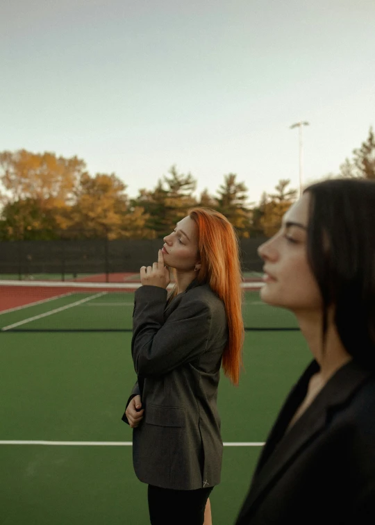 two women, one looking up, stand on a tennis court