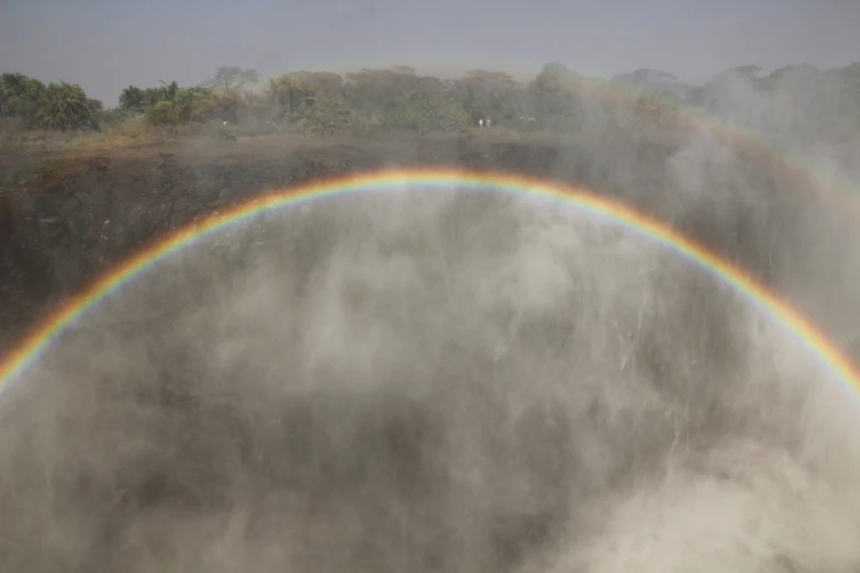 a double rainbow is visible through the clouds over a large hill