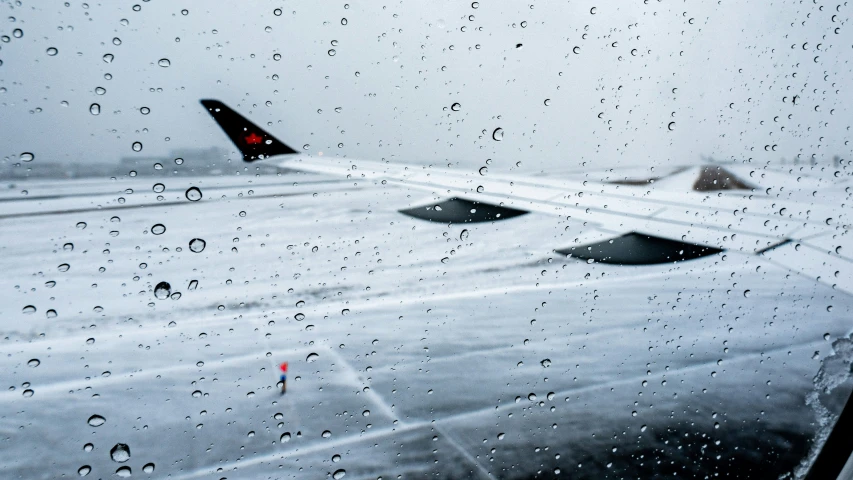 a rain covered window shows a view of an airplane wing