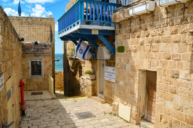 a narrow stone street next to a blue balcony