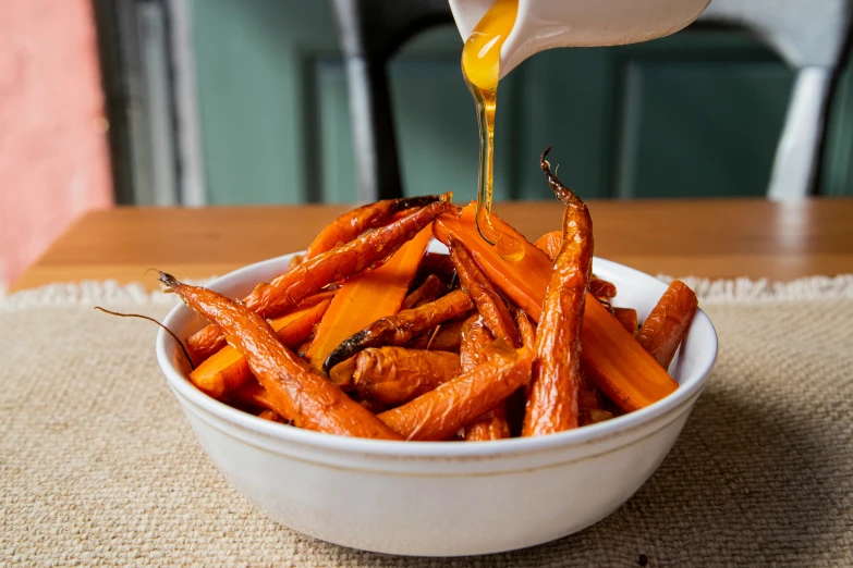 there is sauce pouring into a bowl full of roasted carrots