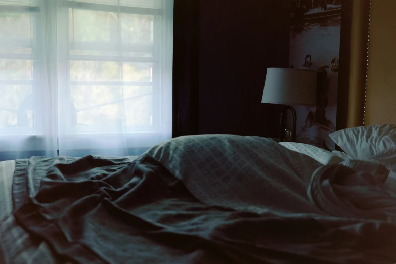 an unmade bed next to a window in the evening