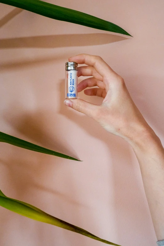 a hand is holding a tiny white bottle on top of leaves