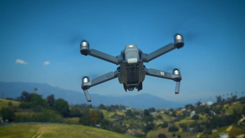 a small grey drone flying over some grass and trees