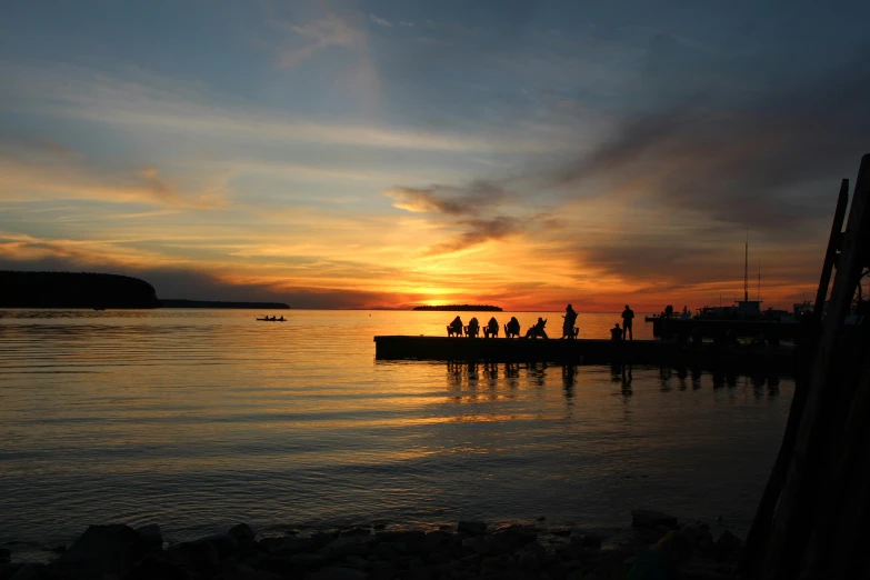 a boat with people standing on the pier watching the sun set