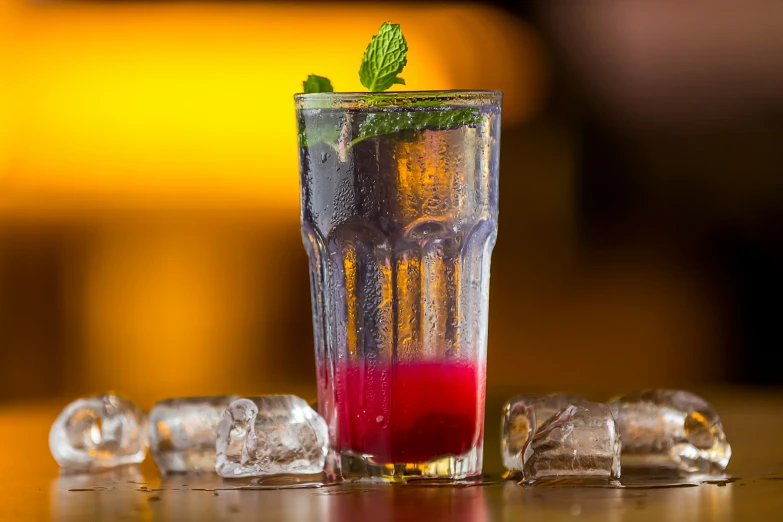 a glass of ice with red liquid and green leaf