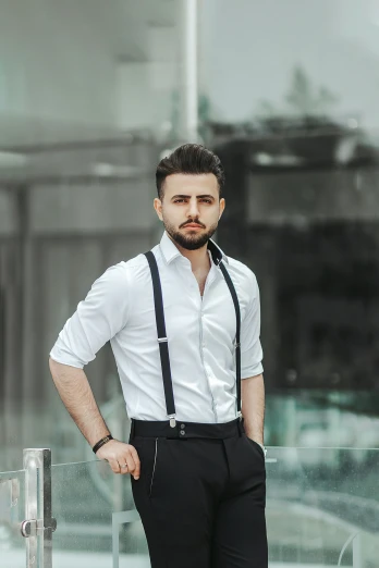 a bearded young man poses in a shirt and slacks