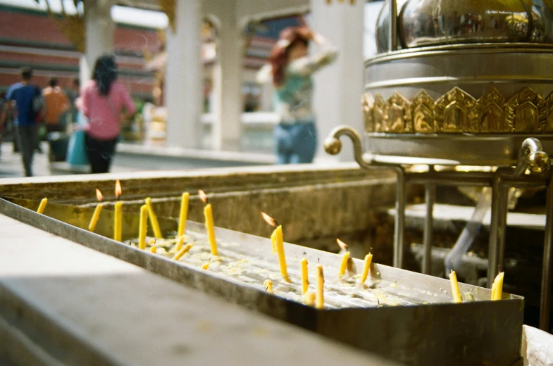 a metal urn with candles and people walking by