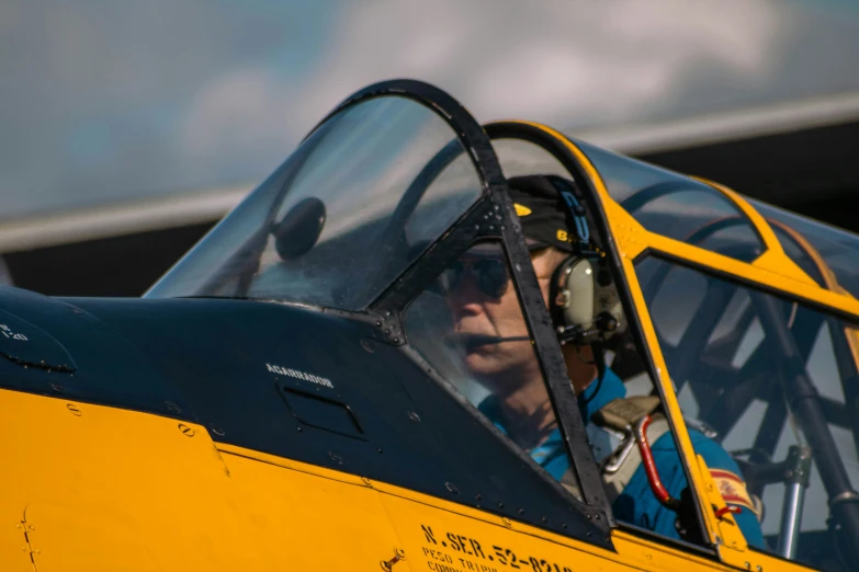 a pilot in a yellow airplane looking out the window