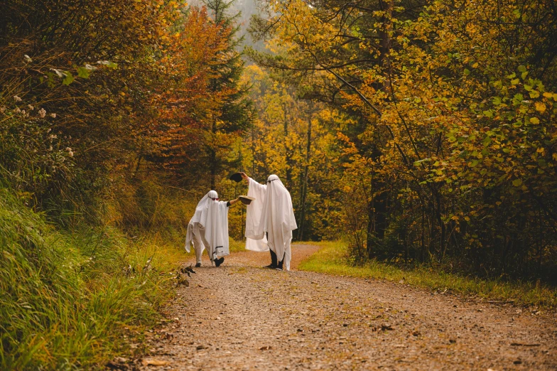 two women dressed in white walking down a road with a scarecrow