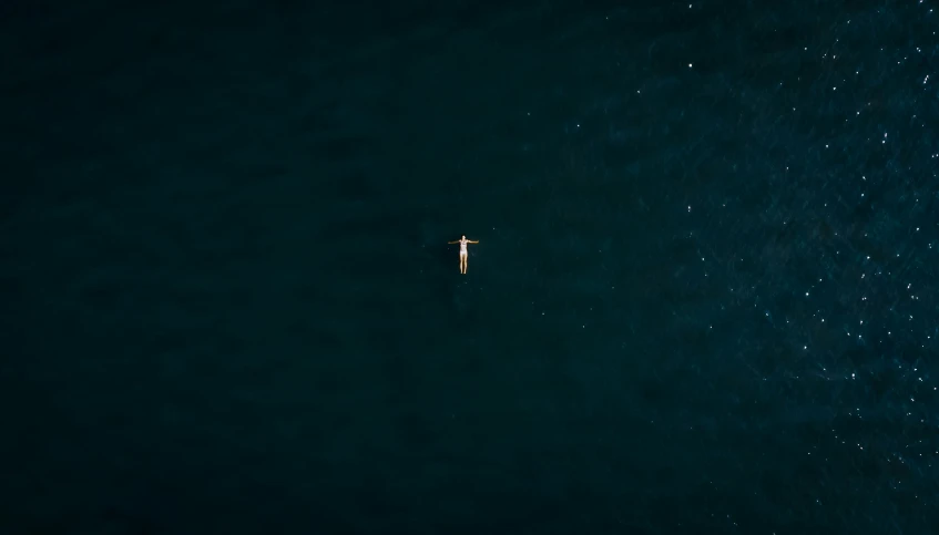 a small boat in the middle of an ocean with a lone surfer