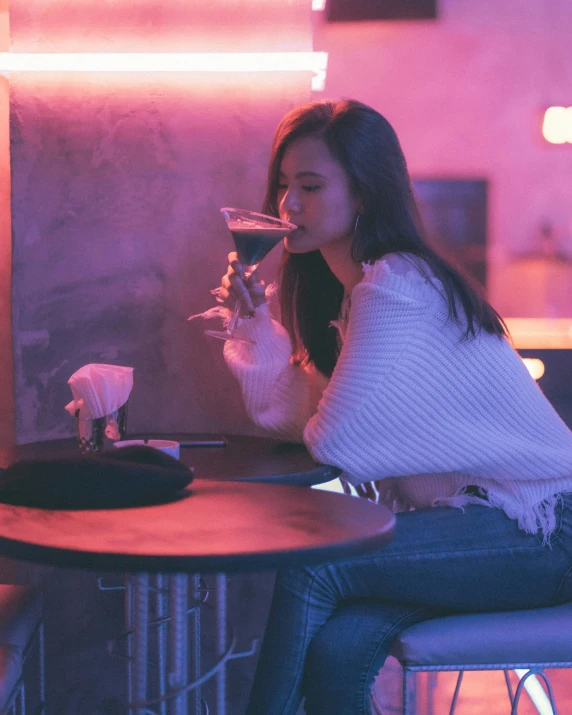 a woman sitting at a table drinking soing from a glass