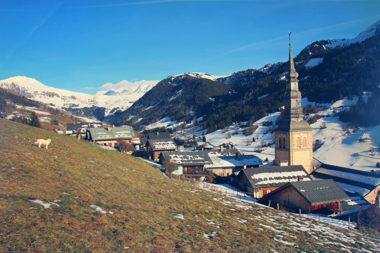 a mountain town with a church steeple and snow covered mountains in the background