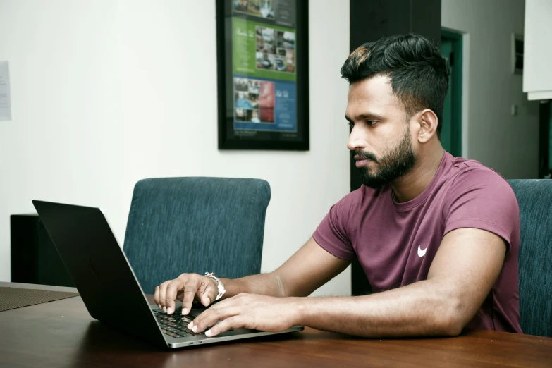 a man in a purple shirt typing on a laptop