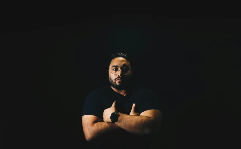 a man in a dark room with his arms crossed looking bored