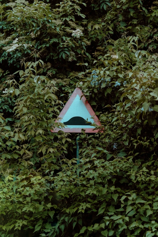 an upside down triangular sign is nestled between a tree
