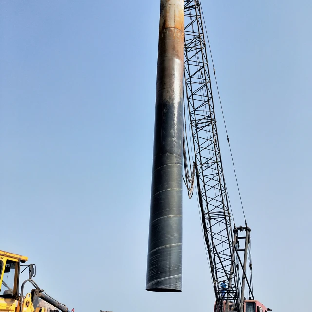 a large crane lifting a giant pipe onto a hill