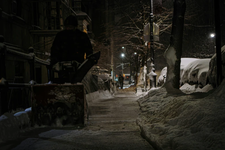 a man rides his skateboard down a snowy sidewalk at night