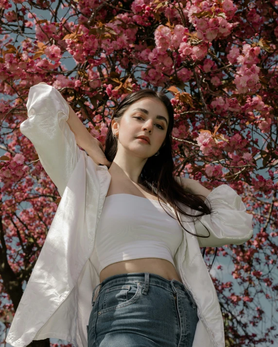 a woman is posing in front of a flowering tree