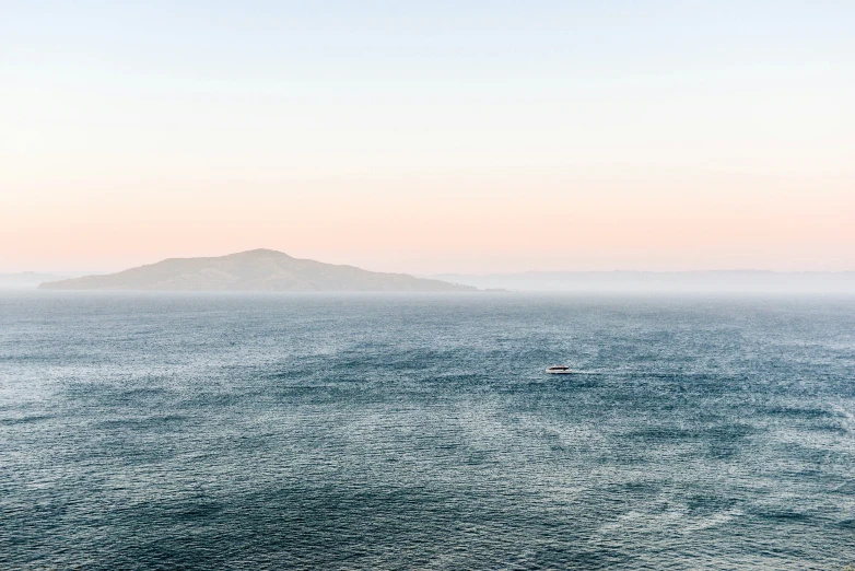 a lone boat on the open water with a small island in the distance