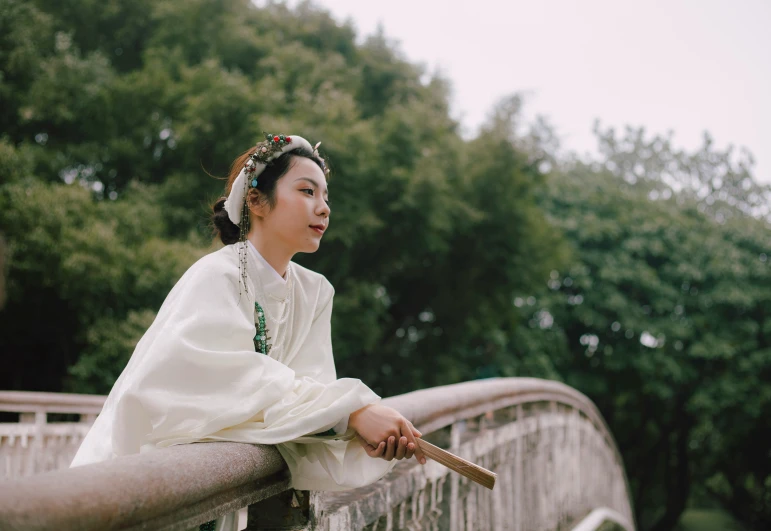 an asian woman in white clothes sitting on a bridge