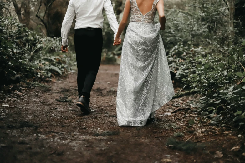 a newlywed couple walking together through a woods holding hands