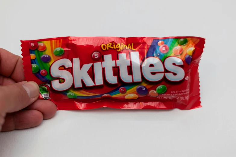 a hand holding a candy bar with skittles