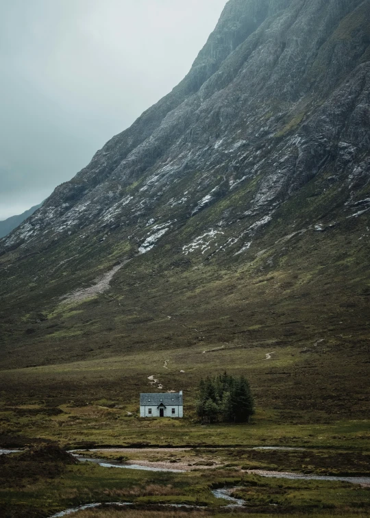 a house sits in a field by a large mountain