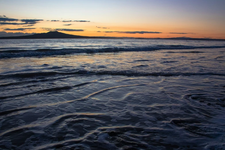 waves are coming in on the beach at sunset