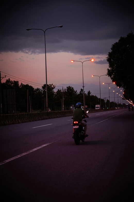 a person riding a motorcycle on the road in front of some street lamps