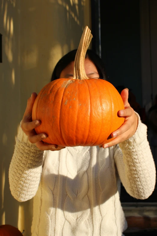 a woman holding up a pumpkin over her eyes