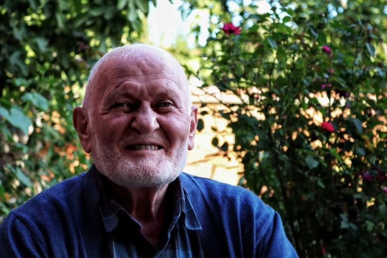 a close - up of an old man, he has a goatee and smiles as if he's on a cellphone