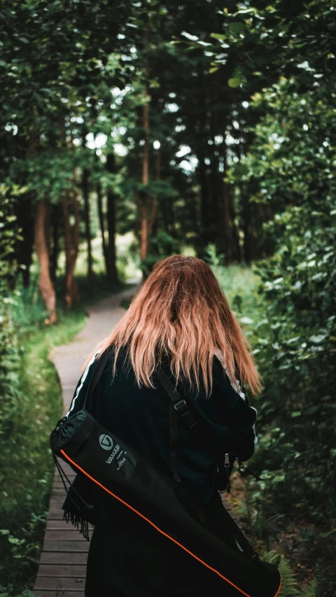 a woman holding a surfboard walking through the woods