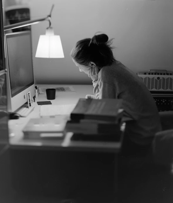 a  sits at a desk by a lamp and computer