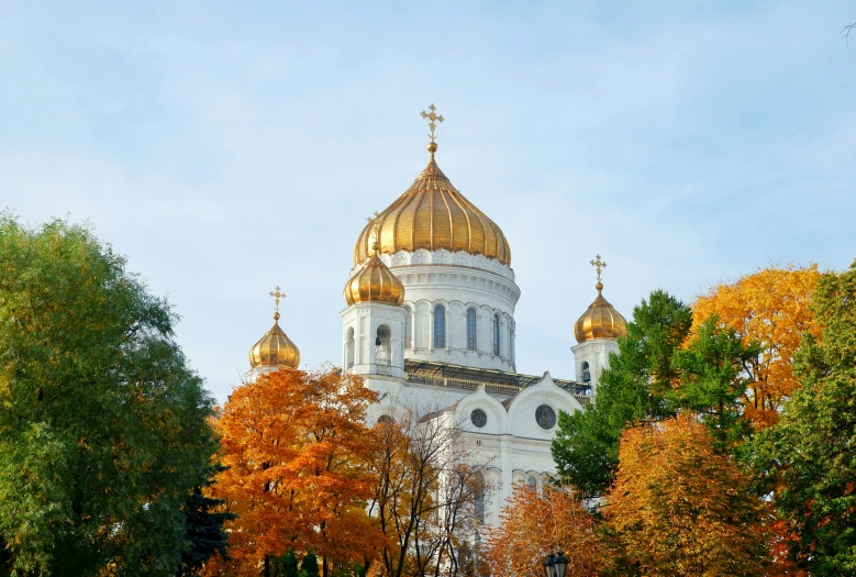 a tall cathedral with gold domes stands next to trees