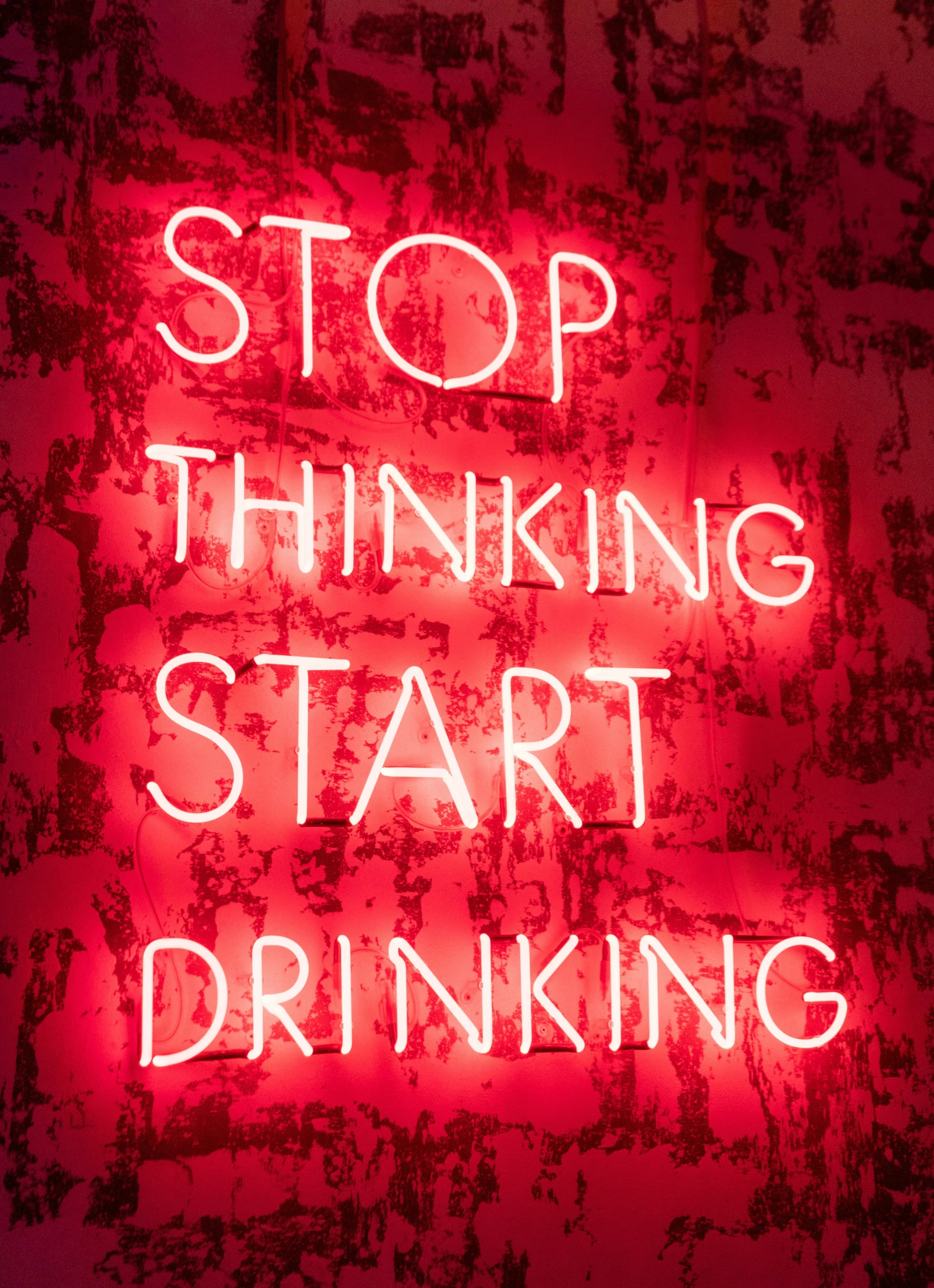 a neon sign reads, stop thinking start drinking