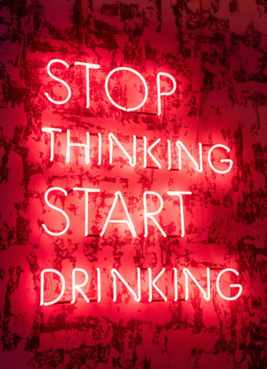 a neon sign reads, stop thinking start drinking