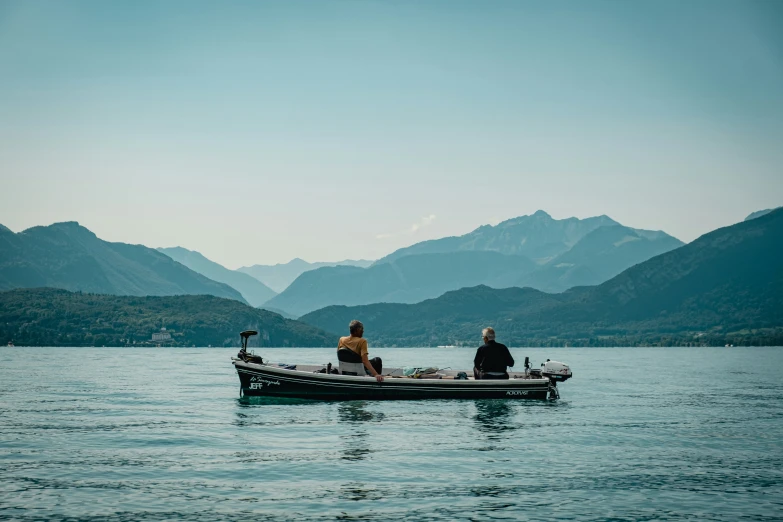 two people in the boat on the water by mountains