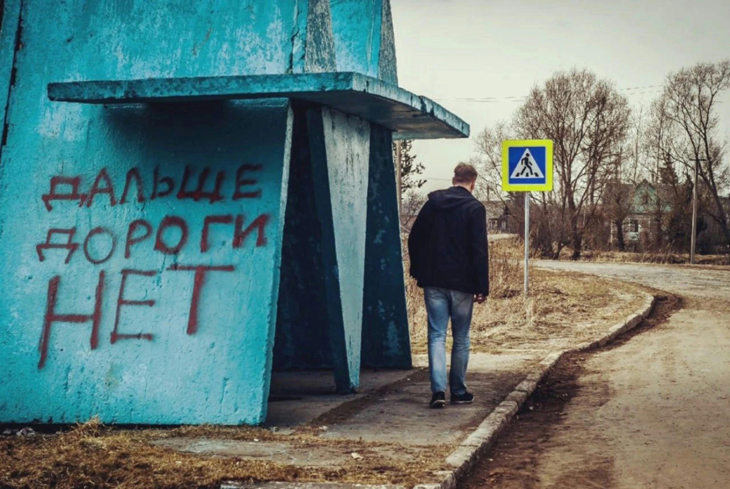 a man walking down a dirt road next to a green building