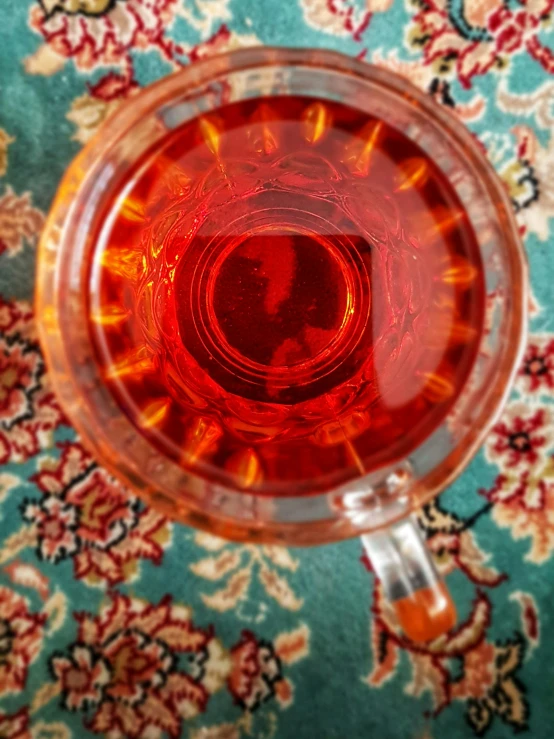 the red liquid in the cup is on the floral tablecloth