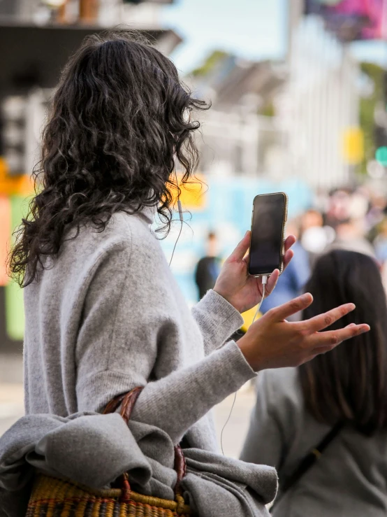 a woman in grey sweater holding up a cellphone