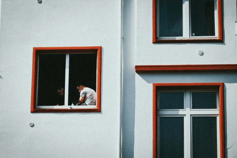 man looking out window in building with red trim