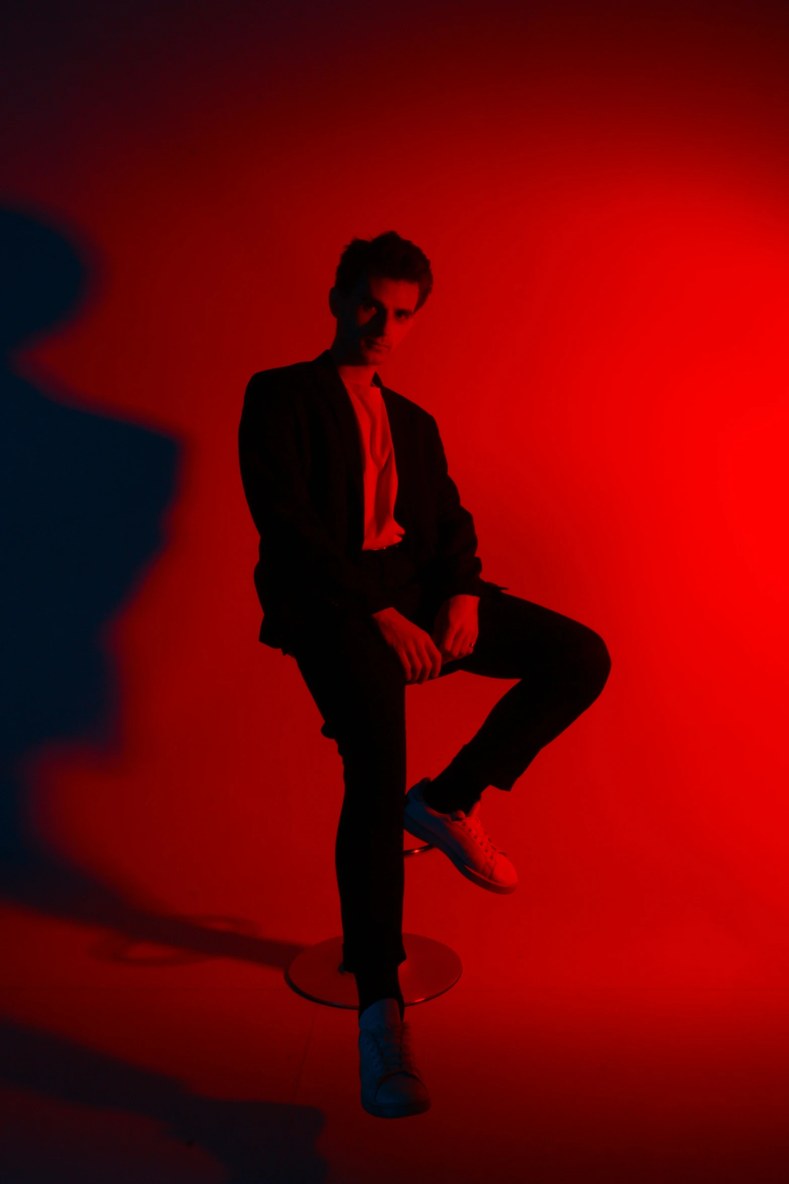 man sitting on round skateboard in red room with blue and white background