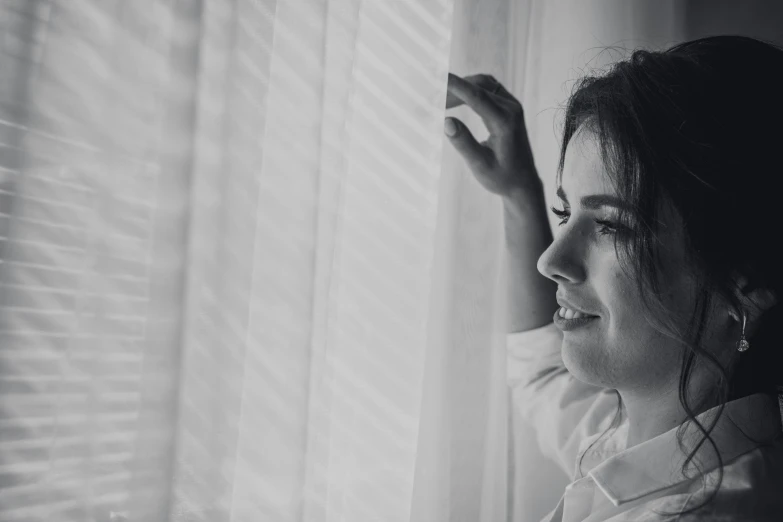 a woman looks out the window as she leans against the curtains
