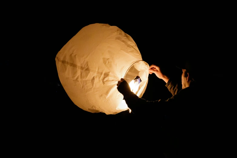 a man lights a paper lantern in the dark