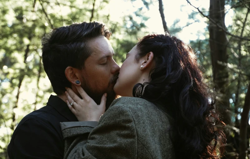 the woman and man are kissing in front of trees